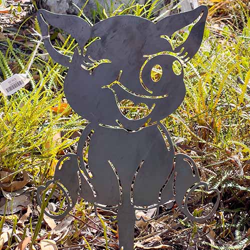 Baby Pig Cartoon Metal Garden Art in Bush Setting Close Up